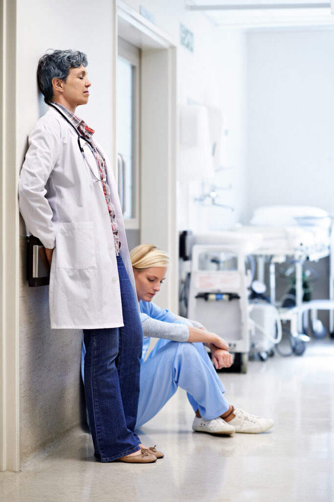 Shot of two exhausted doctors leaning against the wall in a hospital