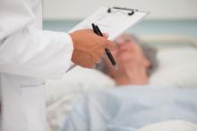 Doctor holds clipboard at elderly patient's bedside.
