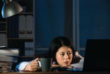 A sleepy doctor holds a coffee mug while looking at her computer.