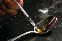 Drug user taking heroin from a spoon with a syringe