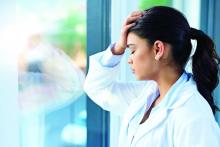 A stressed-out health care provider stands with her hand on her forehead.