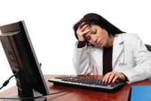A visibly frustrated physician works at a computer.